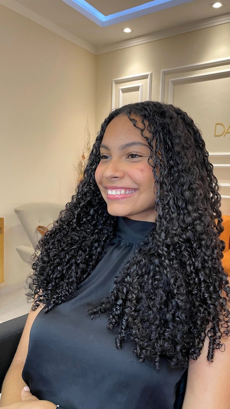 Cliente sorrindo com cabelo longo cacheado no studio.